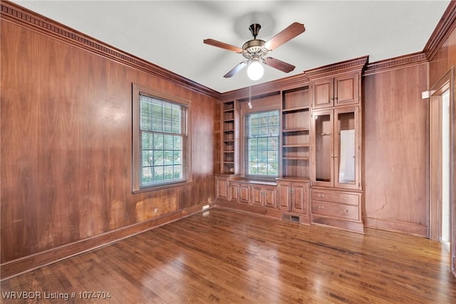 empty room featuring wooden walls, ceiling fan, dark hardwood / wood-style flooring, built in shelves, and crown molding