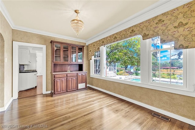 unfurnished dining area featuring crown molding, light hardwood / wood-style flooring, a chandelier, and sink