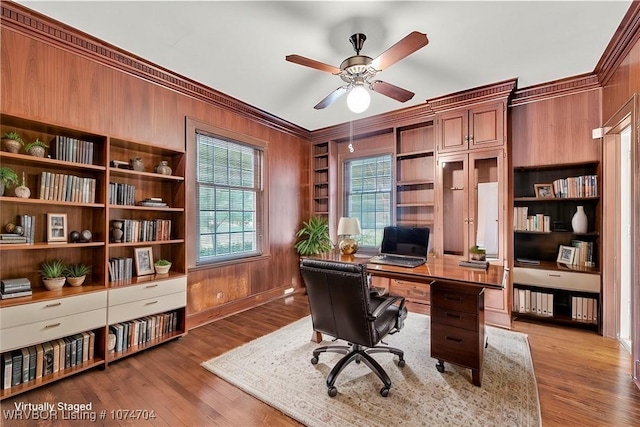 office featuring ceiling fan, built in features, wood-type flooring, wood walls, and crown molding