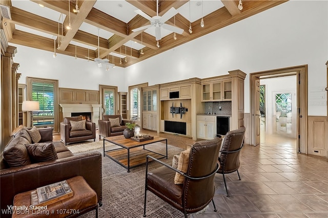 living room featuring ceiling fan, tile patterned floors, coffered ceiling, a high ceiling, and beam ceiling