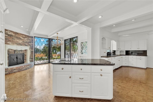 kitchen featuring white cabinets, a fireplace, beamed ceiling, and light parquet floors