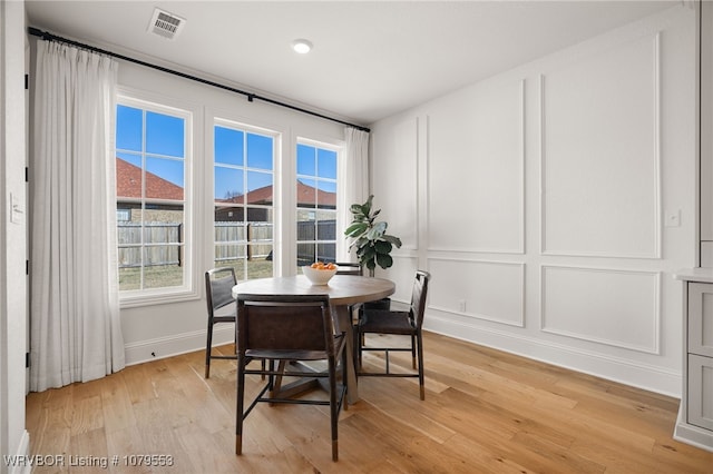 dining space featuring visible vents, light wood finished floors, plenty of natural light, and a decorative wall