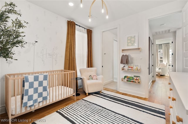 bedroom featuring visible vents, a crib, and light wood-style floors