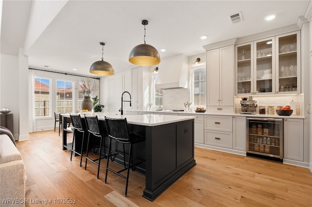 kitchen with premium range hood, visible vents, beverage cooler, light wood-style floors, and light countertops