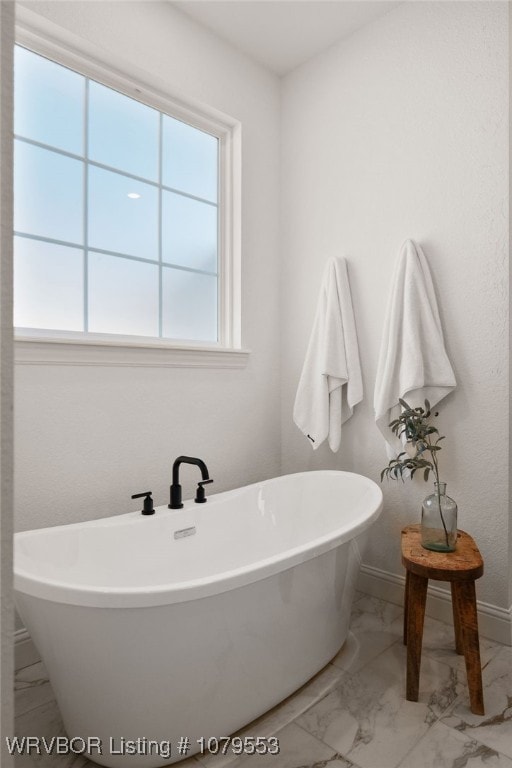 full bathroom with marble finish floor, baseboards, and a freestanding tub