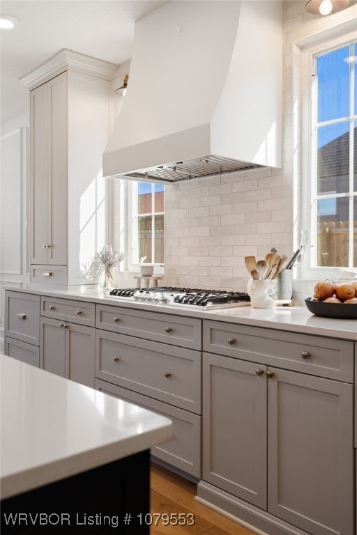 kitchen with light countertops, custom range hood, gray cabinets, and stainless steel gas stovetop