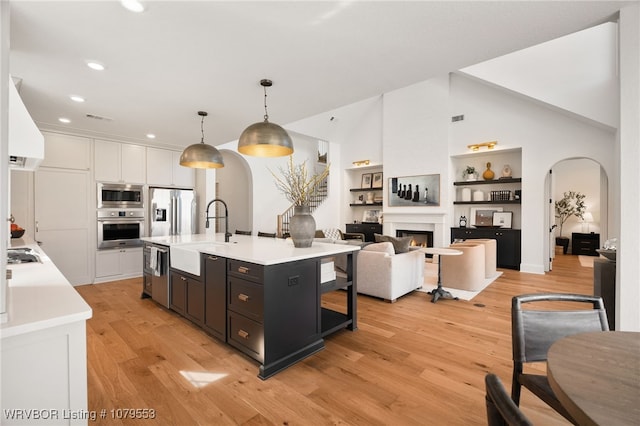 kitchen featuring arched walkways, a sink, stainless steel appliances, light countertops, and light wood-type flooring