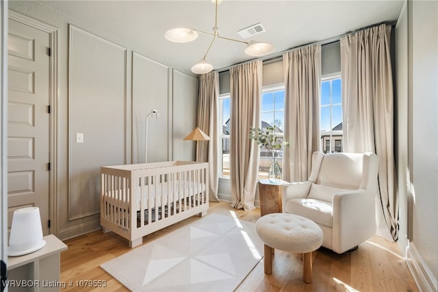 bedroom with visible vents, a nursery area, wood finished floors, and a decorative wall