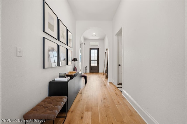 hall featuring light wood-style flooring, baseboards, and arched walkways