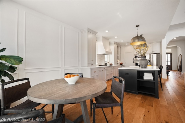 dining room with a decorative wall, recessed lighting, light wood-style flooring, and arched walkways