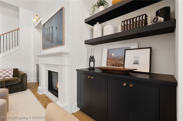 living area with baseboards, light wood-type flooring, and a lit fireplace