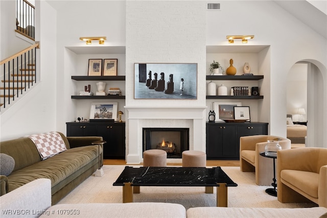 living area featuring light wood finished floors, visible vents, built in shelves, a large fireplace, and arched walkways