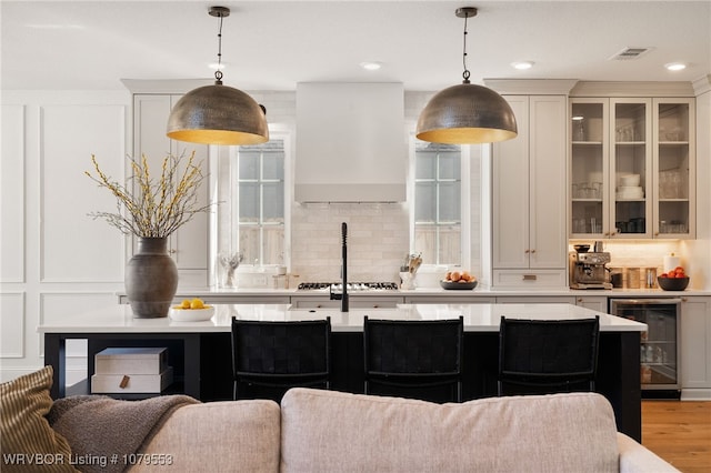 kitchen with visible vents, custom exhaust hood, light countertops, wine cooler, and a decorative wall