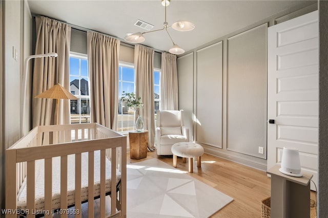 bedroom with a decorative wall, a nursery area, visible vents, and light wood-type flooring