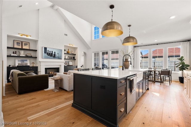 kitchen with light countertops, a warm lit fireplace, dark cabinetry, light wood-style floors, and hanging light fixtures