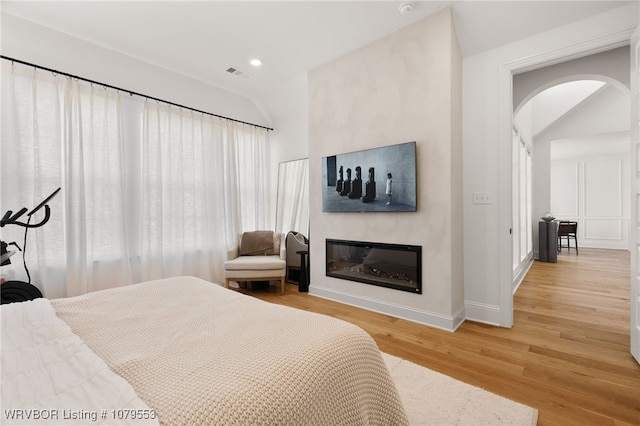 bedroom featuring wood finished floors, visible vents, recessed lighting, arched walkways, and a glass covered fireplace