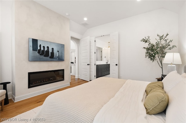 bedroom featuring wood finished floors, visible vents, recessed lighting, vaulted ceiling, and a glass covered fireplace