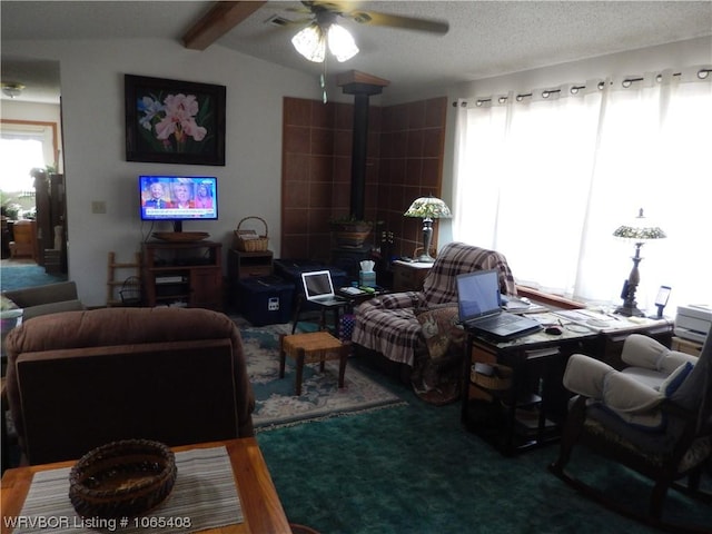 living room with vaulted ceiling with beams, ceiling fan, a wood stove, and a textured ceiling