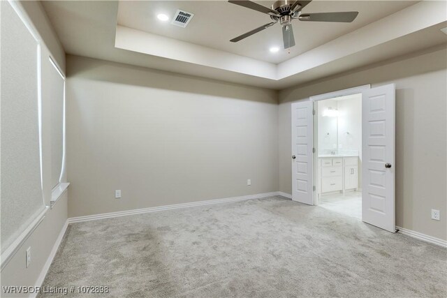 unfurnished bedroom featuring ensuite bathroom, ceiling fan, a raised ceiling, and light colored carpet