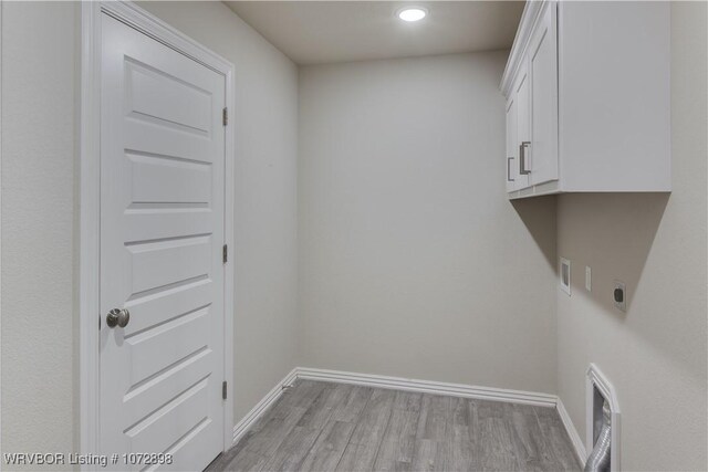 washroom featuring electric dryer hookup, hookup for a washing machine, light hardwood / wood-style flooring, and cabinets