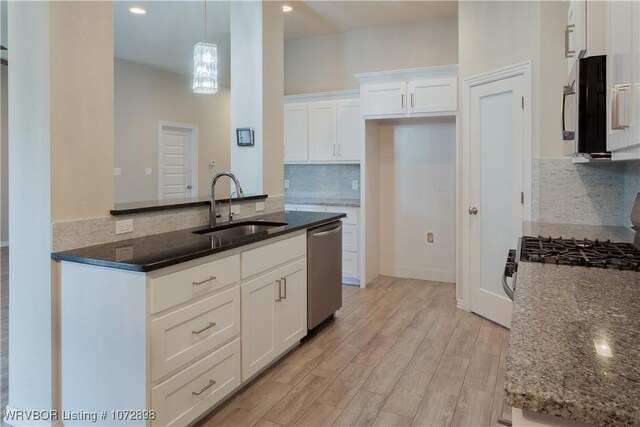 kitchen featuring dark stone counters, sink, stainless steel dishwasher, decorative light fixtures, and white cabinetry