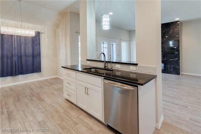 kitchen with stainless steel dishwasher, sink, pendant lighting, dark stone countertops, and white cabinets