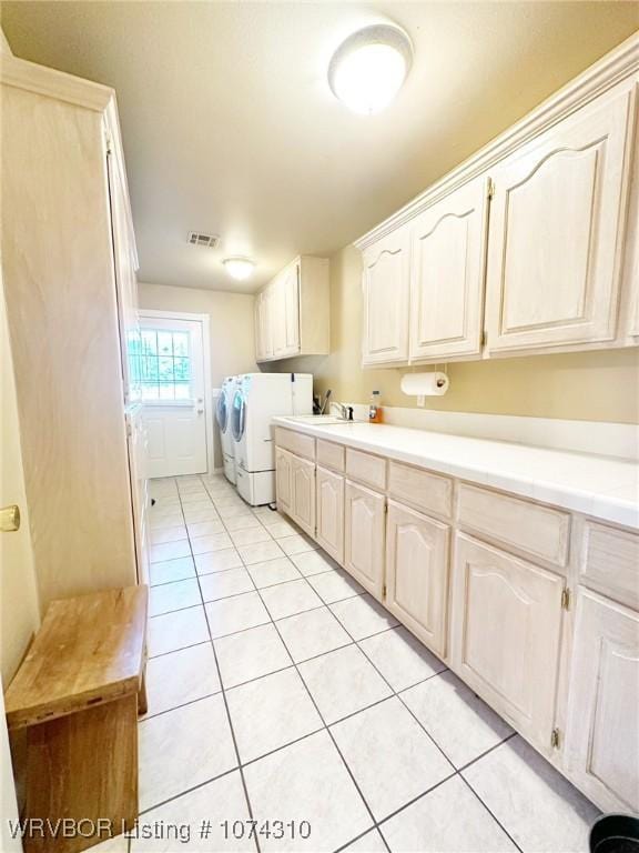 clothes washing area with washer and dryer, sink, light tile patterned floors, and cabinets