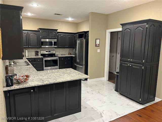 1610 Tiger Lily Ct, Greenwood, AR 72936 - kitchen with stainless steel appliances, a peninsula, light marble finish flooring, decorative backsplash, and dark cabinets
