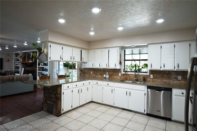 kitchen with light tile patterned floors, sink, dishwasher, white cabinets, and dark stone counters