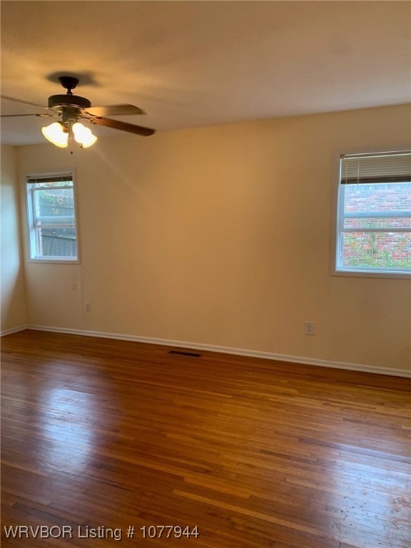 empty room with dark hardwood / wood-style flooring, a wealth of natural light, and ceiling fan