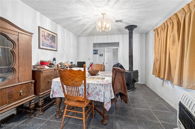 dining space featuring a wood stove, heating unit, a chandelier, and a textured ceiling