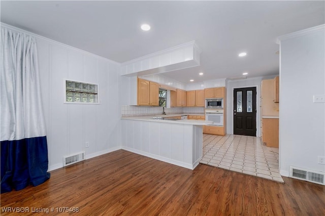 kitchen with stainless steel microwave, light brown cabinets, white oven, kitchen peninsula, and ornamental molding