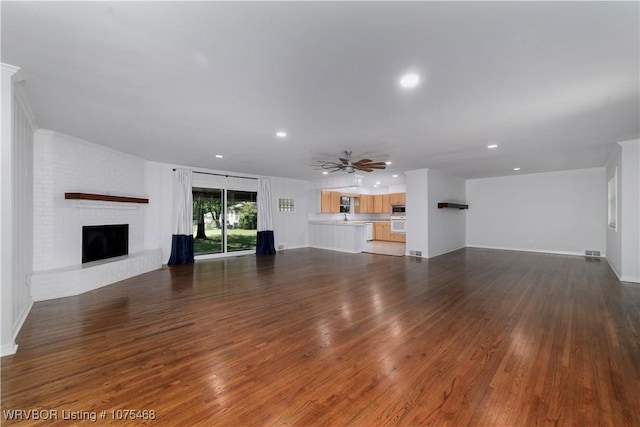 unfurnished living room with ceiling fan, dark hardwood / wood-style flooring, and a brick fireplace