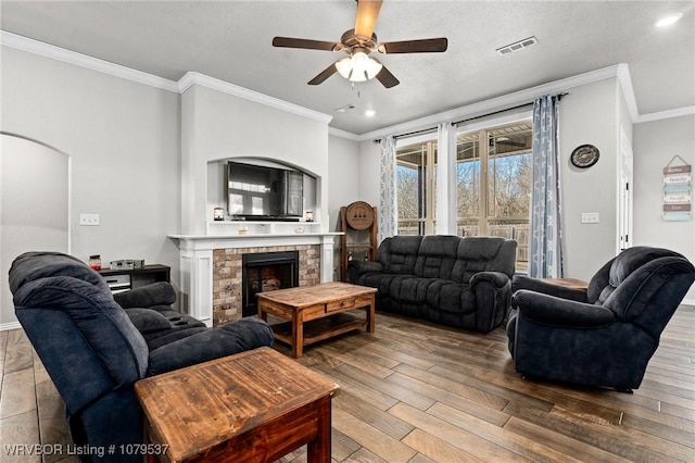 living room featuring visible vents, a brick fireplace, ornamental molding, wood finished floors, and a ceiling fan