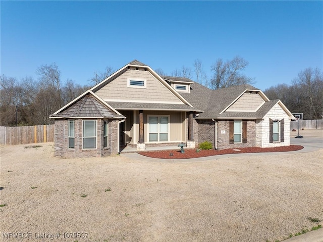 view of front of house with brick siding, a shingled roof, and fence