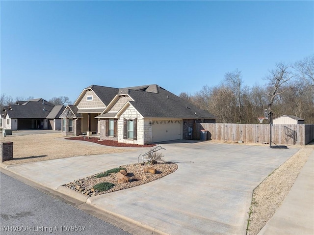 view of front facade featuring stone siding, roof with shingles, concrete driveway, and fence