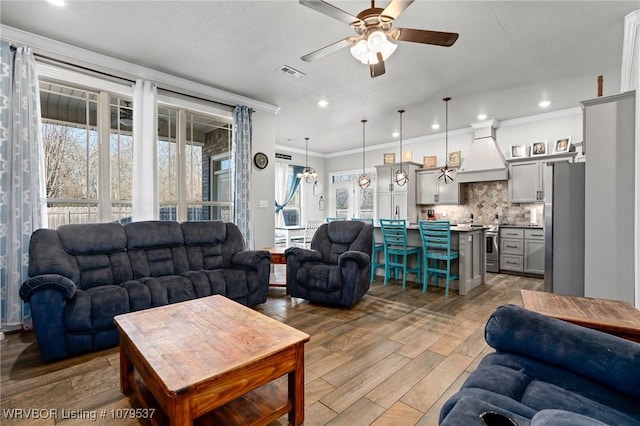 living room with visible vents, light wood-style flooring, recessed lighting, ceiling fan, and crown molding