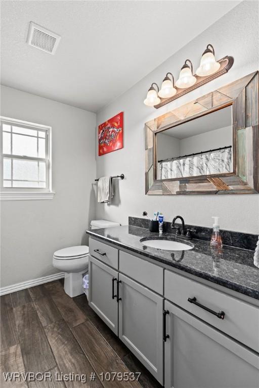 bathroom with visible vents, toilet, wood finished floors, baseboards, and vanity