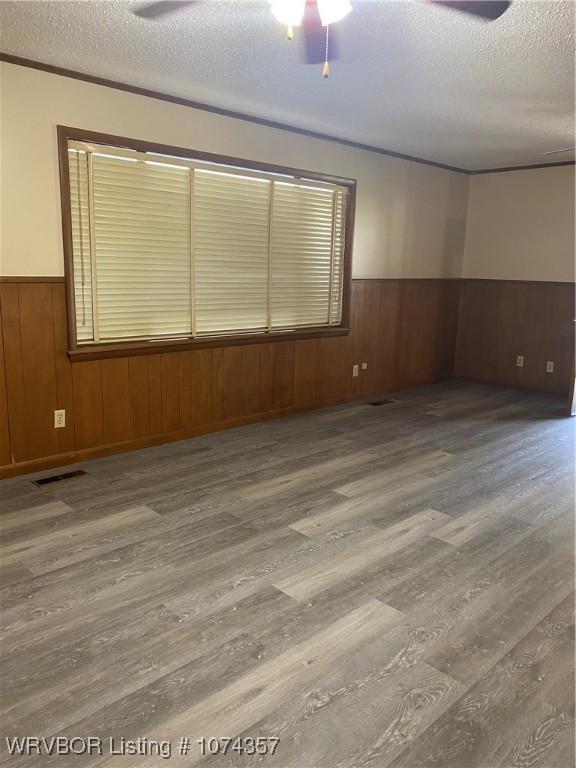 unfurnished room with ceiling fan, wood walls, wood-type flooring, and a textured ceiling