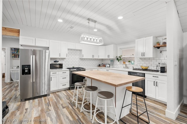 kitchen featuring wood counters, a kitchen island, white cabinetry, stainless steel appliances, and a breakfast bar