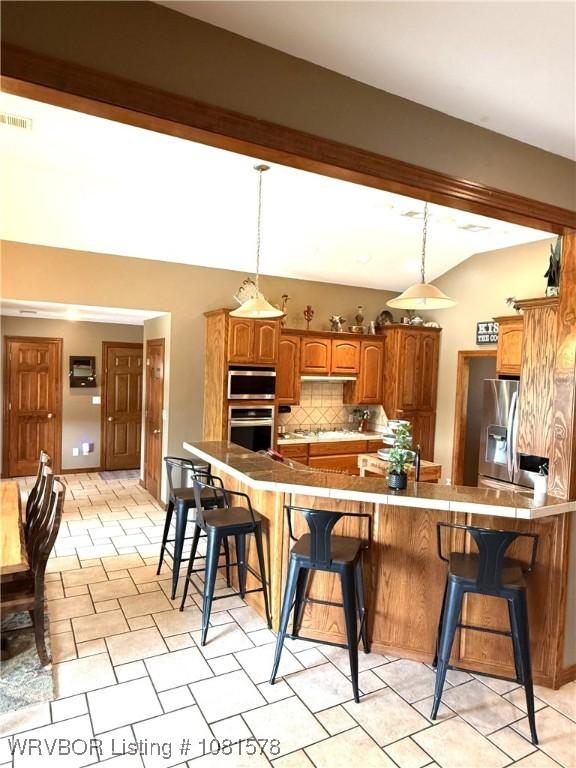417 N Rattlesnake Rd, Charleston, AR 72933 - kitchen featuring appliances with stainless steel finishes, vaulted ceiling, a kitchen bar, decorative backsplash, and brown cabinetry