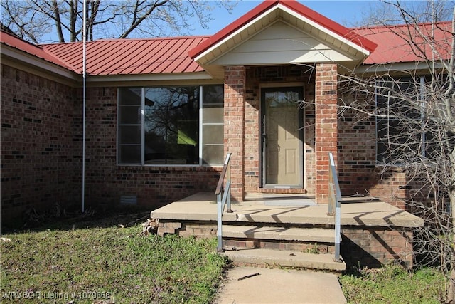 view of exterior entry with crawl space, brick siding, and metal roof
