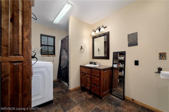 bathroom with washer / clothes dryer, baseboards, stone finish flooring, a tub to relax in, and vanity