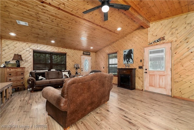 living area featuring wooden walls, lofted ceiling with beams, light wood-style flooring, and visible vents