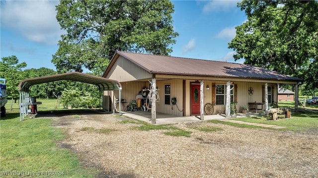 single story home featuring dirt driveway, metal roof, a detached carport, covered porch, and a front yard