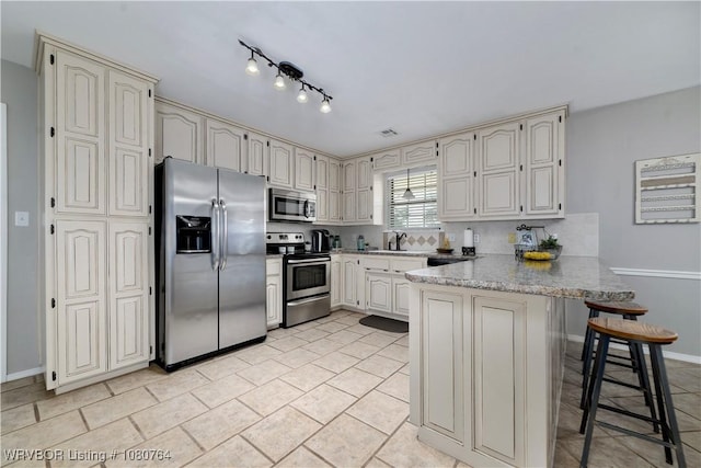 kitchen with a sink, a kitchen breakfast bar, a peninsula, decorative backsplash, and stainless steel appliances