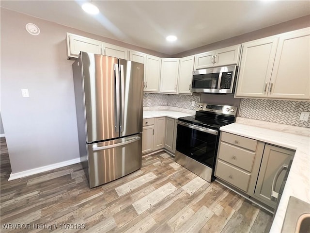 kitchen with baseboards, appliances with stainless steel finishes, backsplash, and wood finished floors