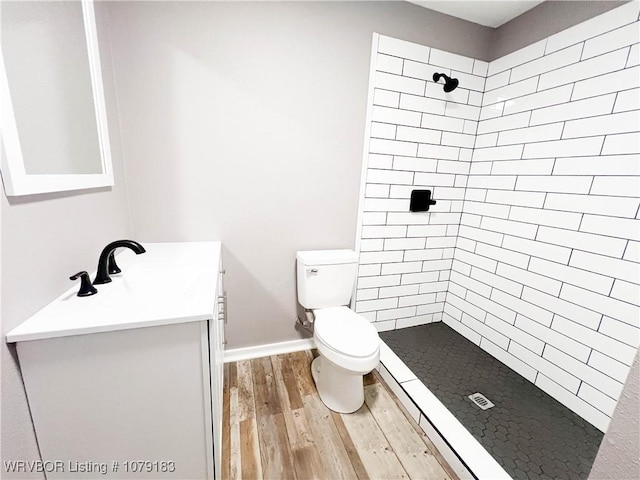 full bath featuring a tile shower, vanity, toilet, and wood finished floors