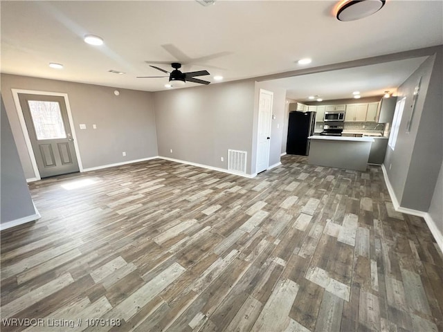 unfurnished living room with a ceiling fan, wood finished floors, visible vents, and baseboards