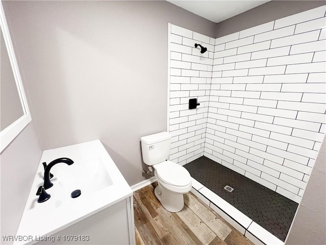 full bathroom featuring a tile shower, vanity, wood finished floors, and toilet